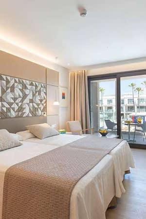 Luxurious hotel room at Barosa Park with a double bed, modern decor, and private balcony overlooking palm trees.