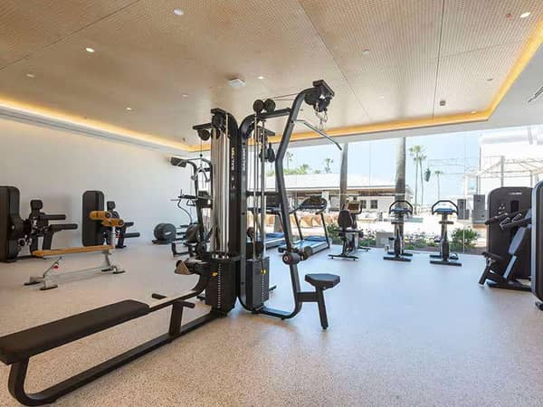 Indoor gym at Barosa Park with exercise bikes, weight benches, and cable machines, illuminated by natural light.