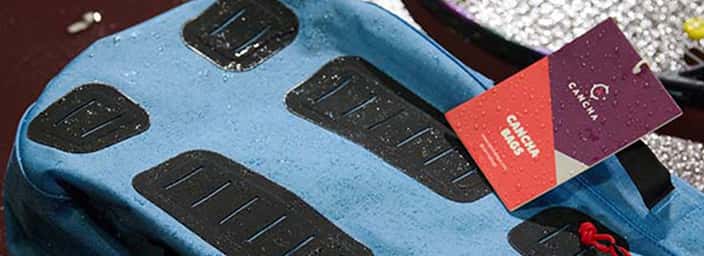 Close-up of a blue CANCHA branded bag with water droplets, featuring black pads and a CANCHA tag highlighting its water-resistant qualities.
