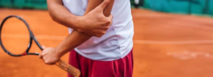 Tennis player holding a racket on a clay court, visible arm suggests muscle tension, wearing white shirt and red shorts.