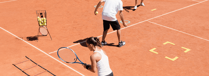 Tennis training session on a clay court with four players, including two women and one man, practising with agility ladders and tennis balls.