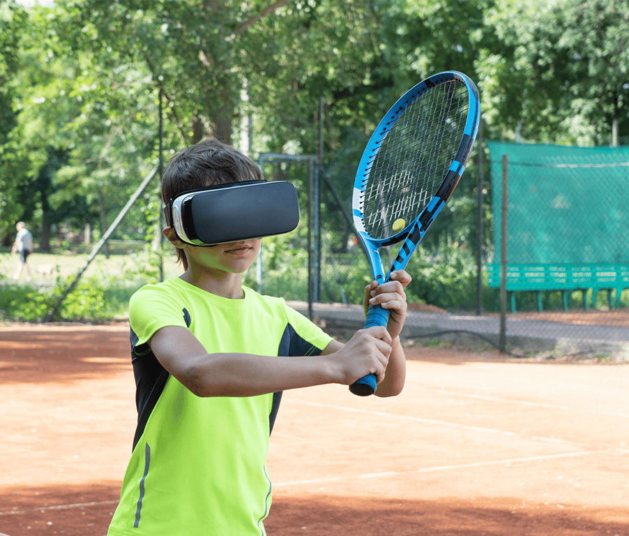 Young boy on a tennis court wearing a VR headset and holding a tennis racket, simulating virtual reality tennis.