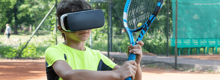 Young boy on a tennis court wearing a VR headset and holding a tennis racket, simulating virtual reality tennis.