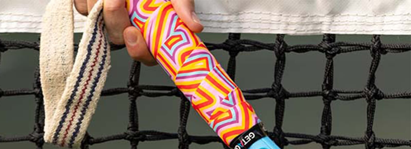 Colourful tennis racket grip with geometric patterns, held in front of a tennis net, from Get a Grip collection.