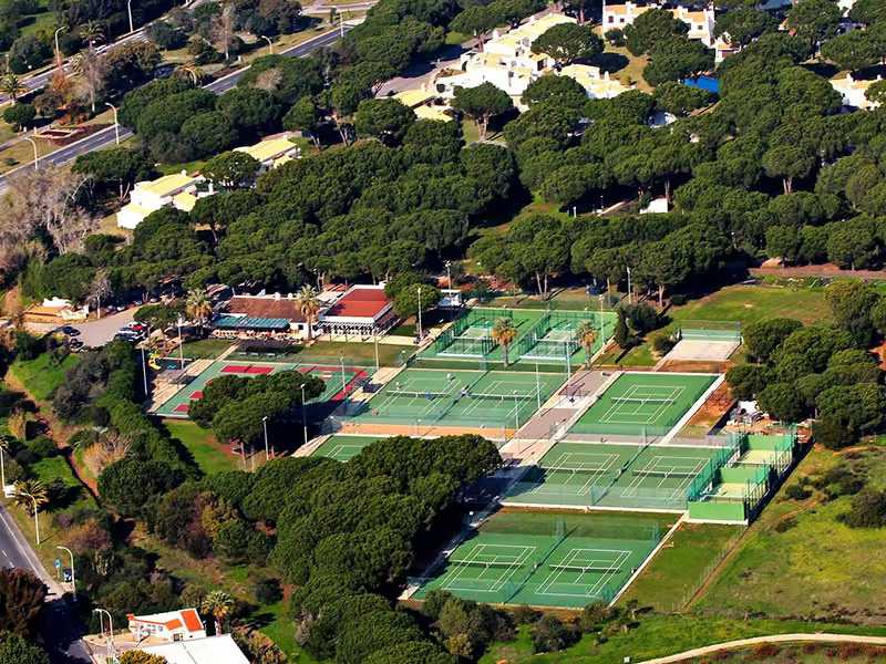 Aerial view of Hilton Vilamoura's tennis courts surrounded by greenery and resort buildings.