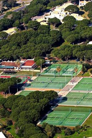 Aerial view of Hilton Vilamoura's tennis courts surrounded by greenery and resort buildings.