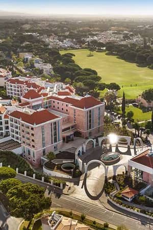 Aerial view of Hilton Vilamoura As Cascatas Golf Resort & Spa, featuring the hotel buildings with red-tiled roofs and an adjacent golf course in lush green surroundings.