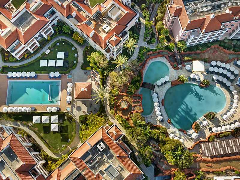 Aerial view of Hilton Vilamoura featuring two large outdoor pools, sun loungers, landscaped gardens, and hotel buildings.