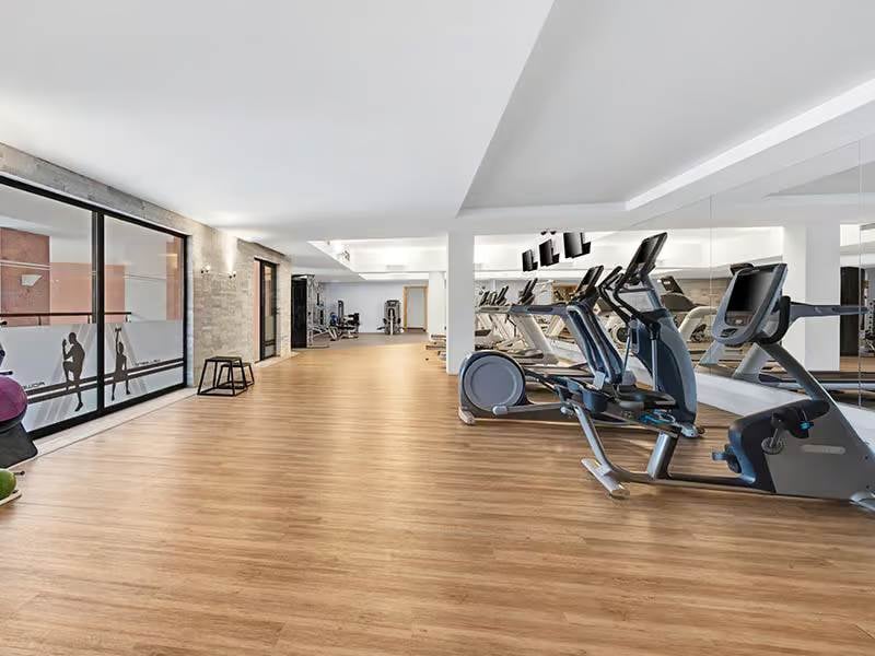 Spacious indoor gym at Hilton Vilamoura with modern exercise equipment including treadmills and elliptical trainers, featuring large windows and wooden flooring.