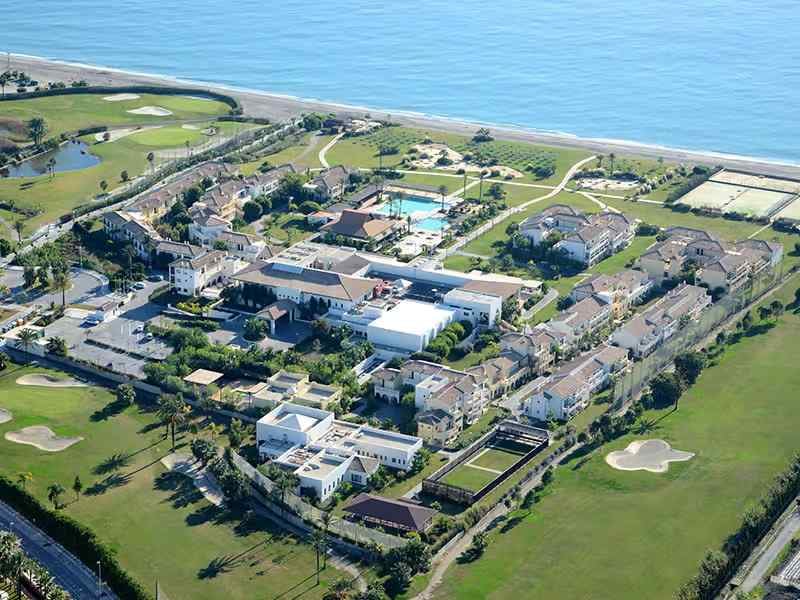 Aerial view of a beachside hotel with resort buildings, swimming pool, green lawns, and ocean access.