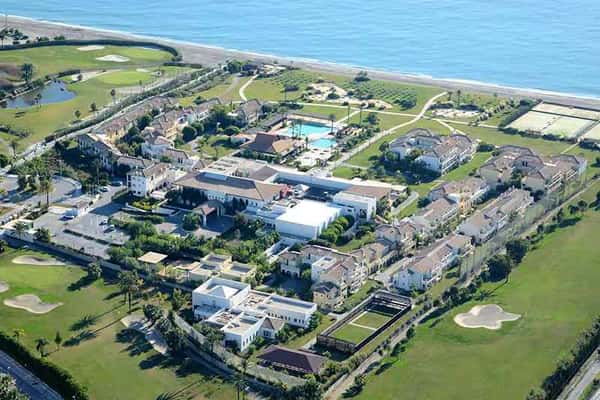 Aerial view of a beachside hotel with resort buildings, swimming pool, green lawns, and ocean access.