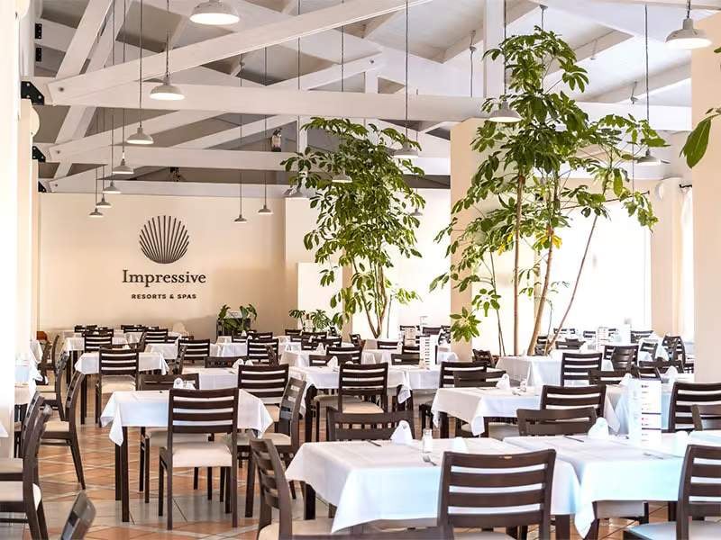 Impressive Resorts & Spas dining area with white tablecloths, dark wooden chairs, green plants, and modern lighting.