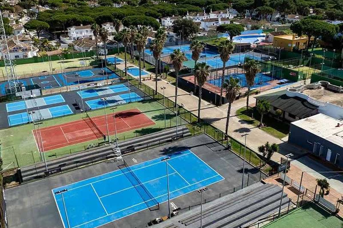Aerial view of Hotel Vincci's tennis courts with various surfaces, surrounded by trees and nearby buildings.