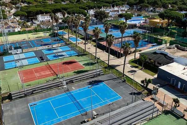 Aerial view of Hotel Vincci's tennis courts with various surfaces, surrounded by trees and nearby buildings.