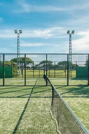 Padel tennis court with green artificial grass and metal fencing at Hotel Vincci, with palm trees and a blue sky in the background.