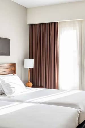 Hotel room with a double bed, wooden headboard, white linens, brown curtains, and natural light at Vincci Gallery Hotel.