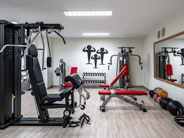 Hotel Vincci's indoor gym area with a multi-use gym machine, red weight bench, dumbbells and kettlebells.