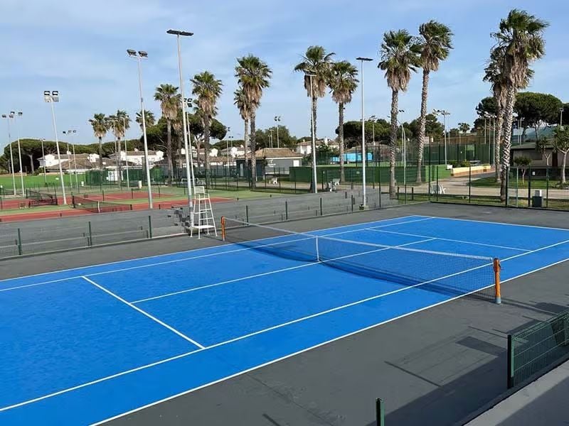 Bright blue tennis court under a clear sky at Hotel Vincci, surrounded by palm trees and additional courts.