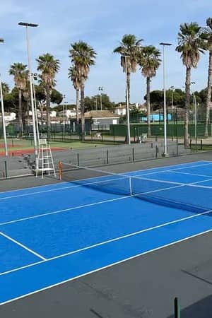 Bright blue tennis court under a clear sky at Hotel Vincci, surrounded by palm trees and additional courts.