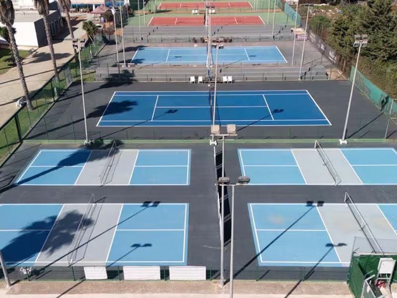 Wide shot of several blue and red tennis courts at Hotel Vincci with clear white markings and surrounding nets.