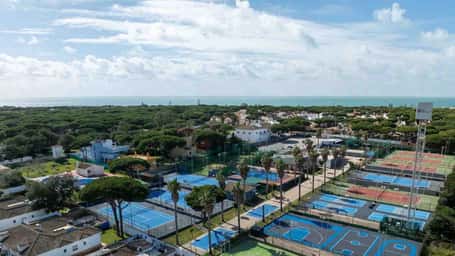 Aerial view of tennis courts surrounded by greenery and residential buildings at Hotel Vincci, under a bright blue sky.