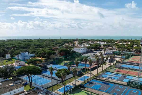 Aerial view of tennis courts surrounded by greenery and residential buildings at Hotel Vincci, under a bright blue sky.