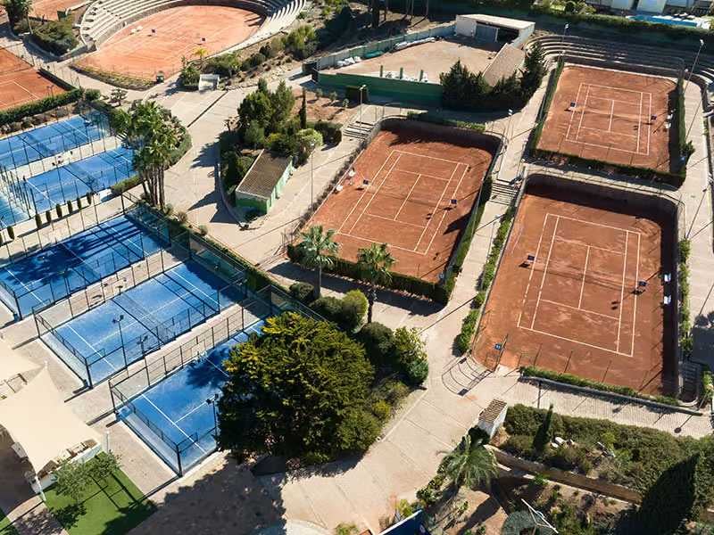 Aerial view of clay tennis courts and blue paddle courts at La Manga Club surrounded by greenery.