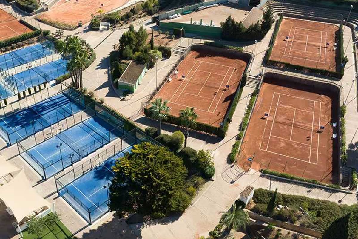Aerial view of clay tennis courts and blue paddle courts at La Manga Club surrounded by greenery.
