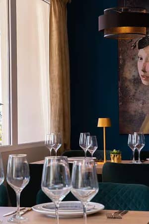 Chic dining area with elegantly set tables, golden lamps, and a wall art piece of a woman with flowers in her hair.