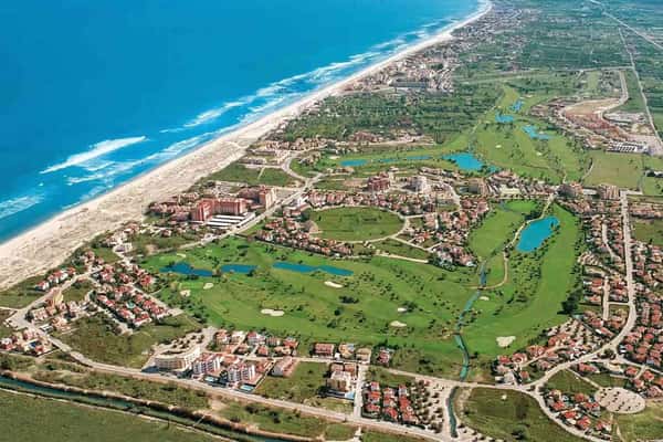 Aerial view of Oliva Nova Golf & Beach Resort with beachfront, golf course, hotel, and surrounding landscape north of Denia, Spain.