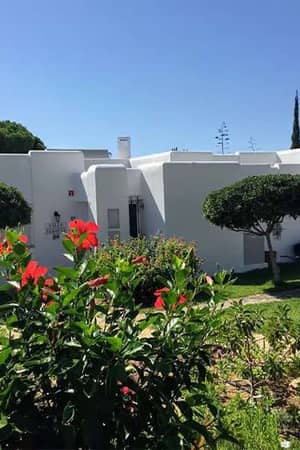 Prado Vilamoura Gallery Hotel Villas exterior with white geometric buildings, lush lawns, and red hibiscus flowers.