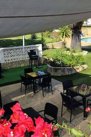 Outdoor poolside lounge area at Prado Vilamoura with shaded seating, bougainvillea flowers, and a swimming pool with sun loungers.