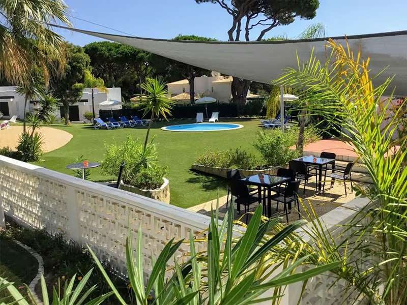 Wide shot of Prado Vilamoura featuring a pool surrounded by sun loungers, lush greenery, and outdoor seating under a canopy.