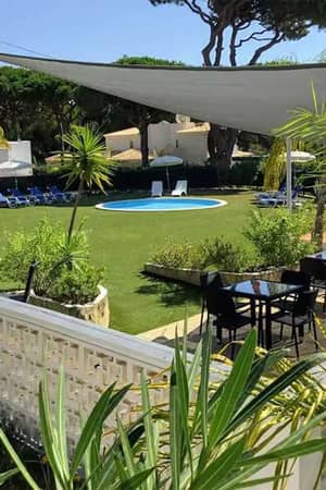 Wide shot of Prado Vilamoura featuring a pool surrounded by sun loungers, lush greenery, and outdoor seating under a canopy.