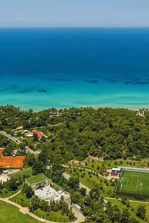 Aerial view of tennis courts at Sani Beach School, with greenery and the ocean in the background.