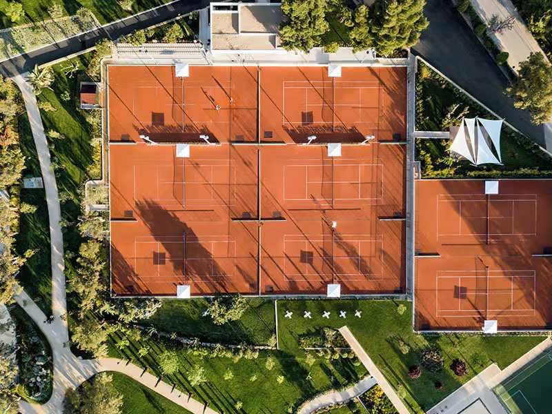 Aerial view of clay tennis courts at Sani Beach School, surrounded by trees and landscaped paths.