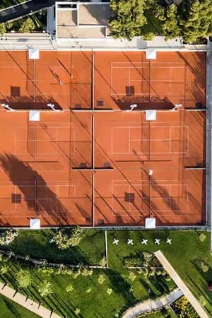 Aerial view of clay tennis courts at Sani Beach School, surrounded by trees and landscaped paths.