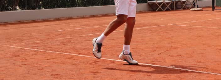 Tennis player wearing stylish shoes on a clay court, capturing movement and athletic footwear design.