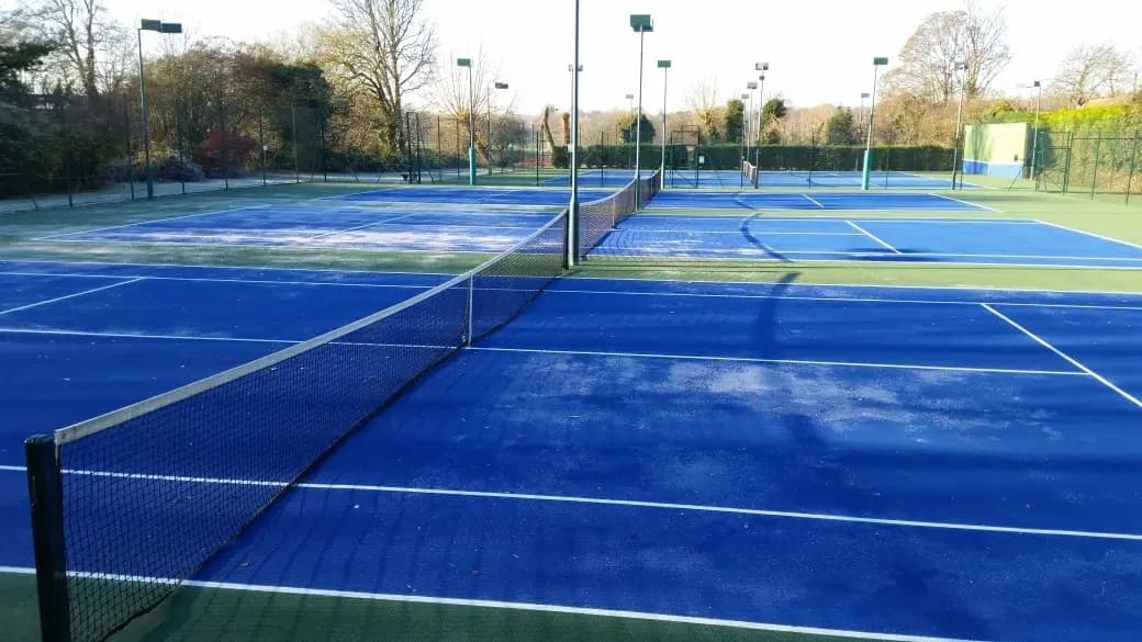 Tennis courts with a light frost covering, surrounded by bare trees, on a clear winter morning.