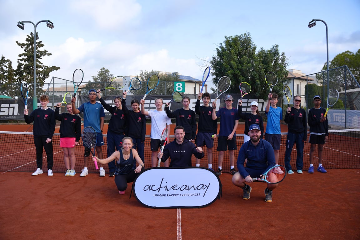 Group of junior players and coaches holding rackets on a clay court with an Active Away sign.