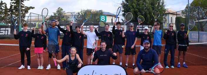 Group of junior players and coaches holding rackets on a clay court with an Active Away sign.