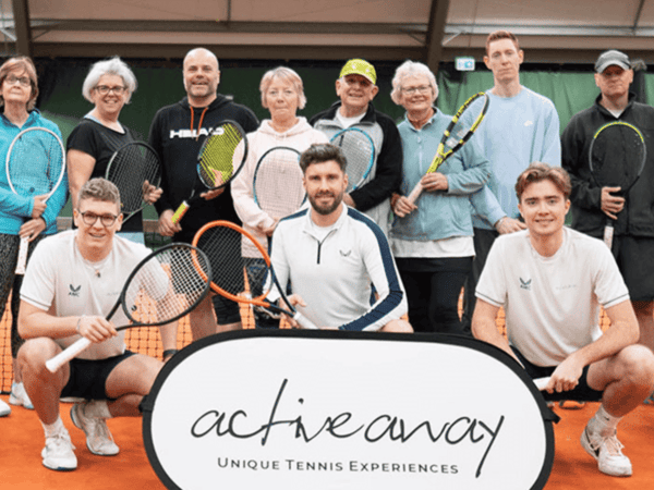 Group of tennis players and coaches on an indoor court behind an Active Away sign.