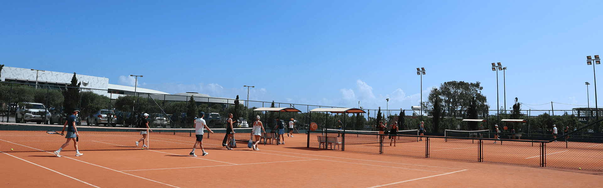 Group tennis session on clay courts under a clear blue sky at a holiday resort.