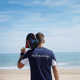 Man holding a padel racket on his shoulder, facing the sea, wearing an Active Away shirt.