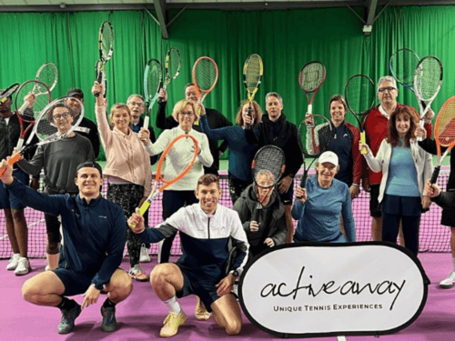 Group of smiling adults holding tennis rackets on an indoor court with an Active Away banner