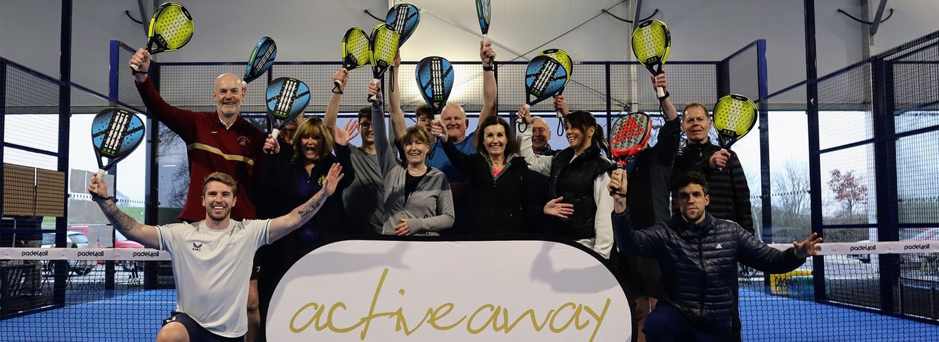 Group celebrating on an indoor padel court, holding rackets aloft behind an Active Away banner.