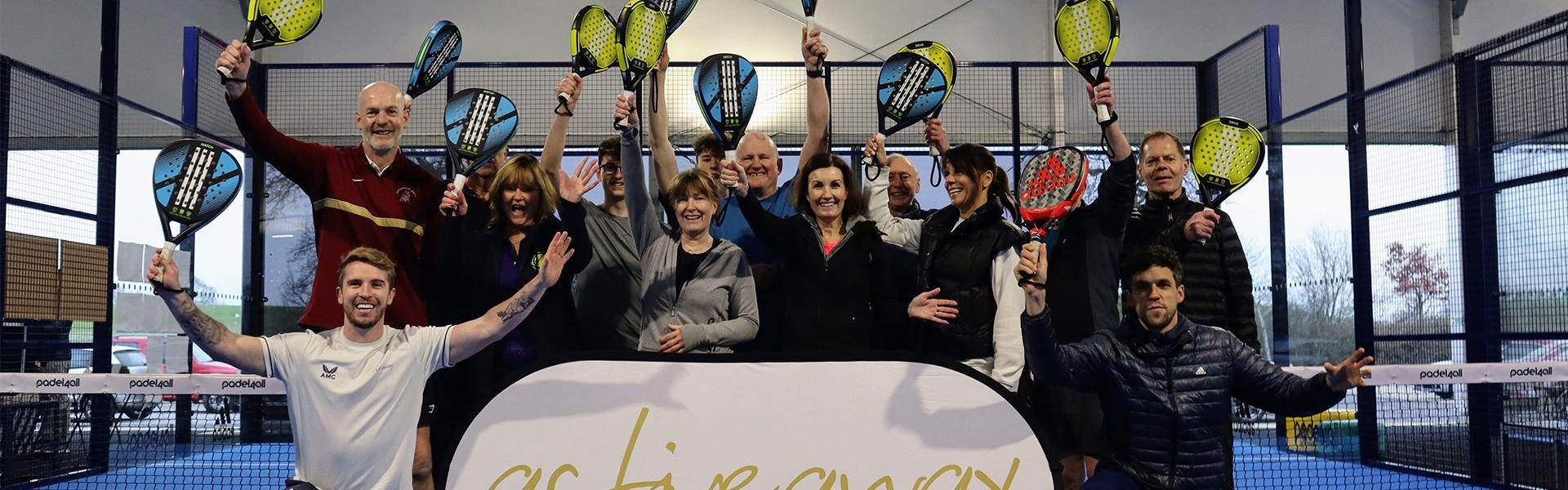 Group celebrating on an indoor padel court, holding rackets aloft behind an Active Away banner.