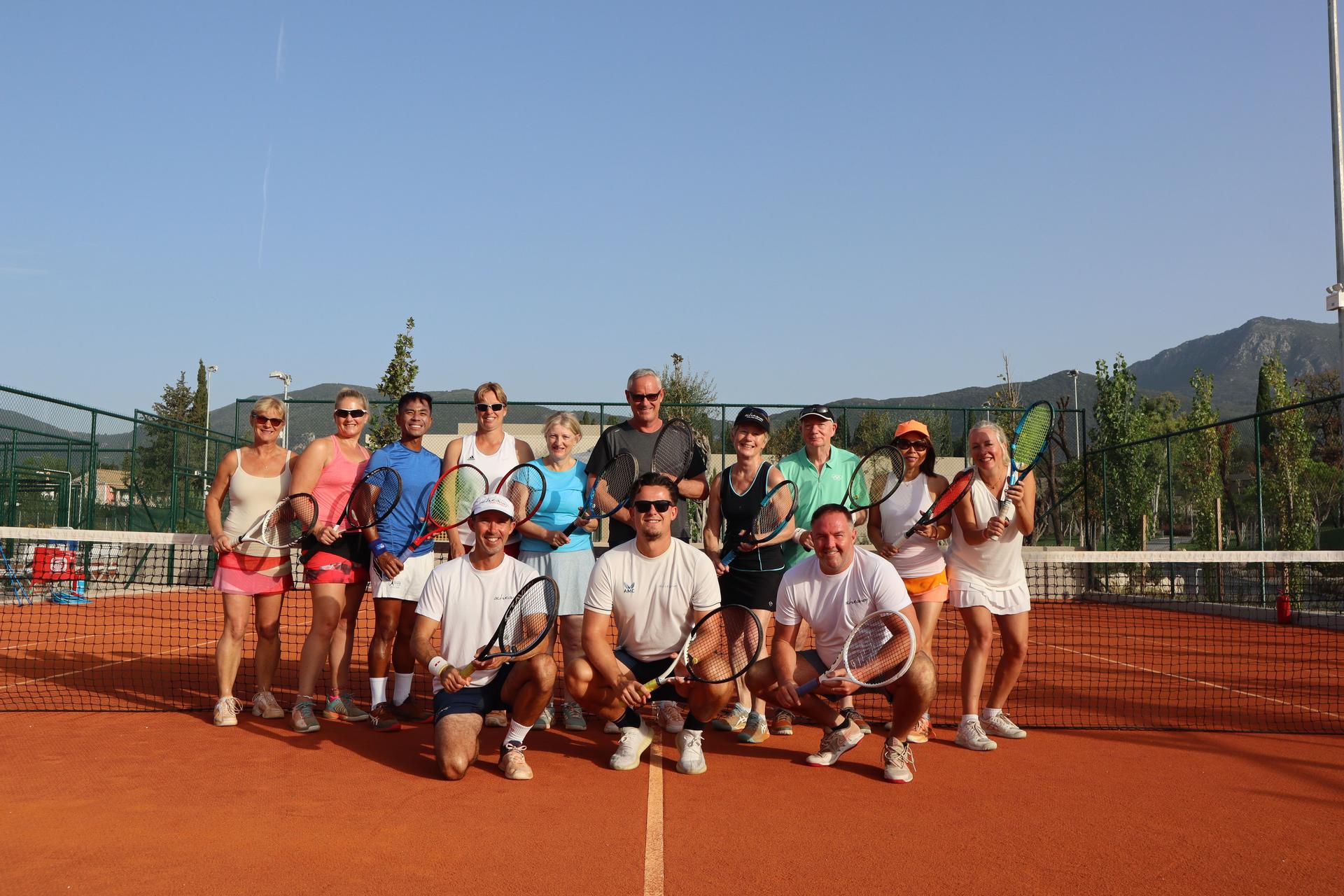 Group of tennis players and coaches posing with rackets on a clay court during an Active Away holiday.
