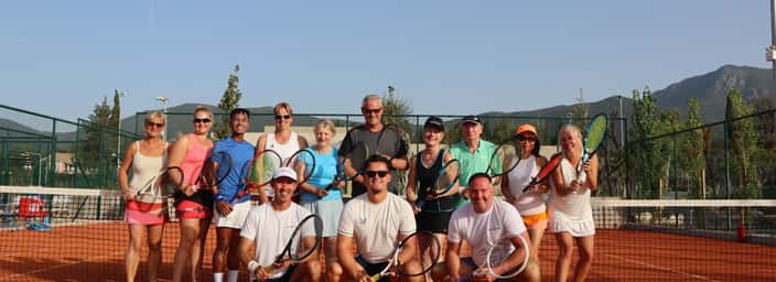 Group of tennis players and coaches posing with rackets on a clay court during an Active Away holiday.