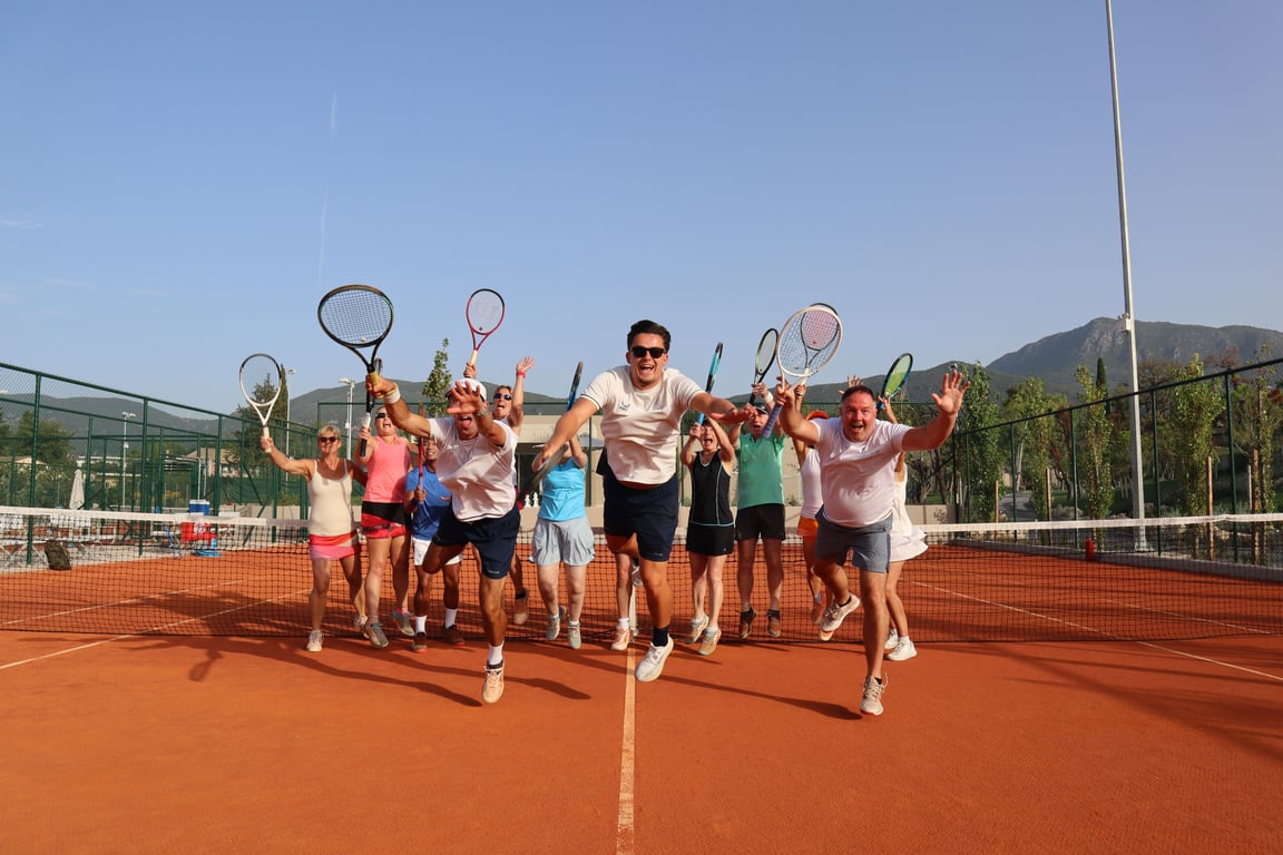 Group of adults jumping with tennis rackets on a clay court, celebrating during an Active Away holiday session.